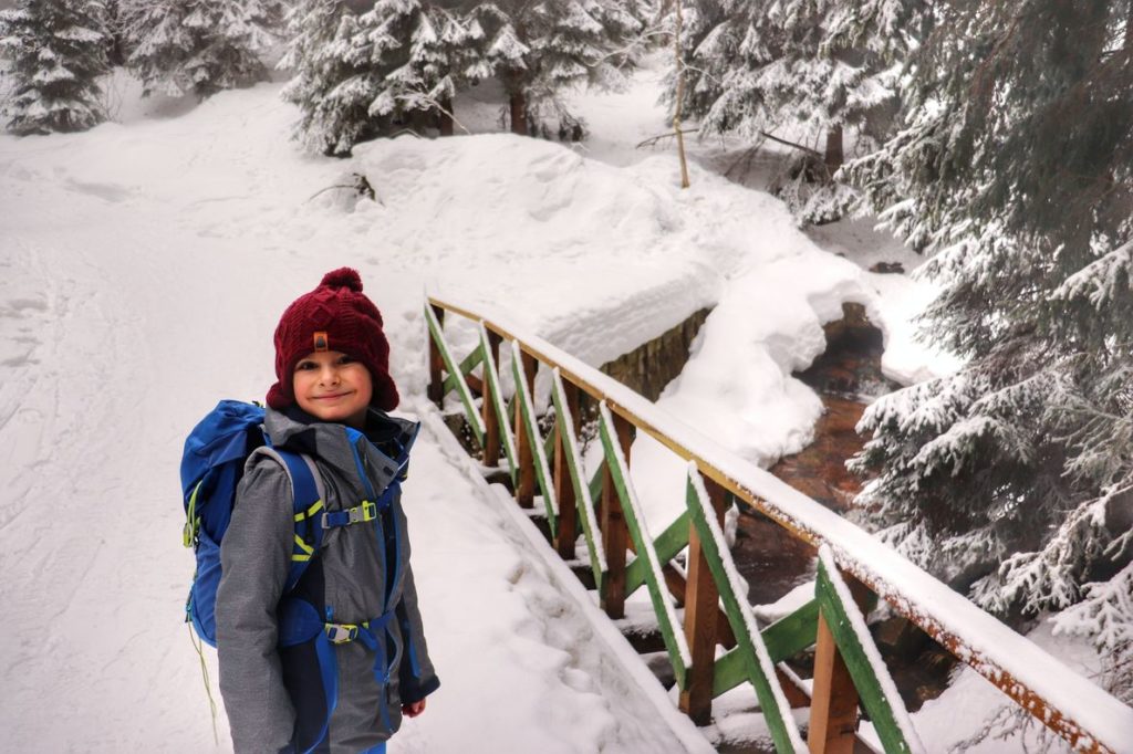 Uśmiechnięte dziecko na drewnianym mości zasypanym przez śnieg na żóltym szlaku w Szklarskiej Porębie