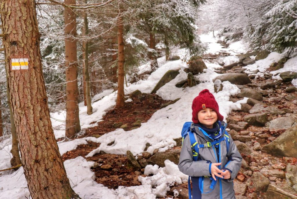 Uśmiechnięte dziecko na żółtym szlaku w Karkonoskim Parku Narodowym, leśna, kamienista ścieżka, pokryta śniegiem
