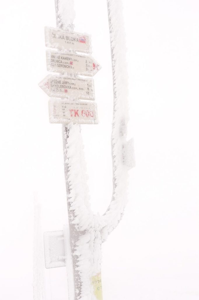 Zmrożony, ledwo widoczny drogowskaz z białą tabliczką z napisem Česká Budka 1417 m n.p.m. - skrzyżowanie szlaków