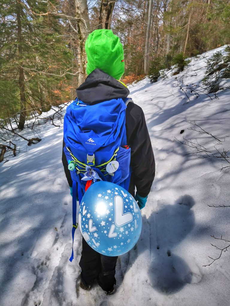 Dziecko idące wąską ścieżką leśną, chłopiec ma przywiązany do plecaka balon z liczbą 7