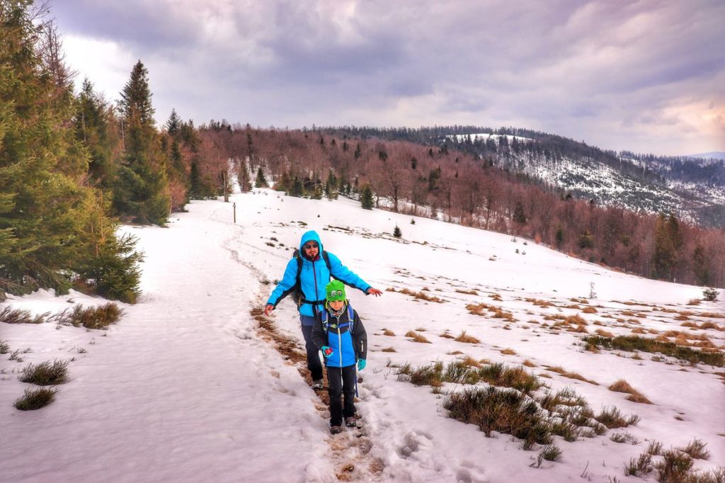 Mały turysta - dziecko z tatą idące wzdłuż zaśnieżonej Hali Kamińskiego, zachmurzone niebo, wiosenny dzień