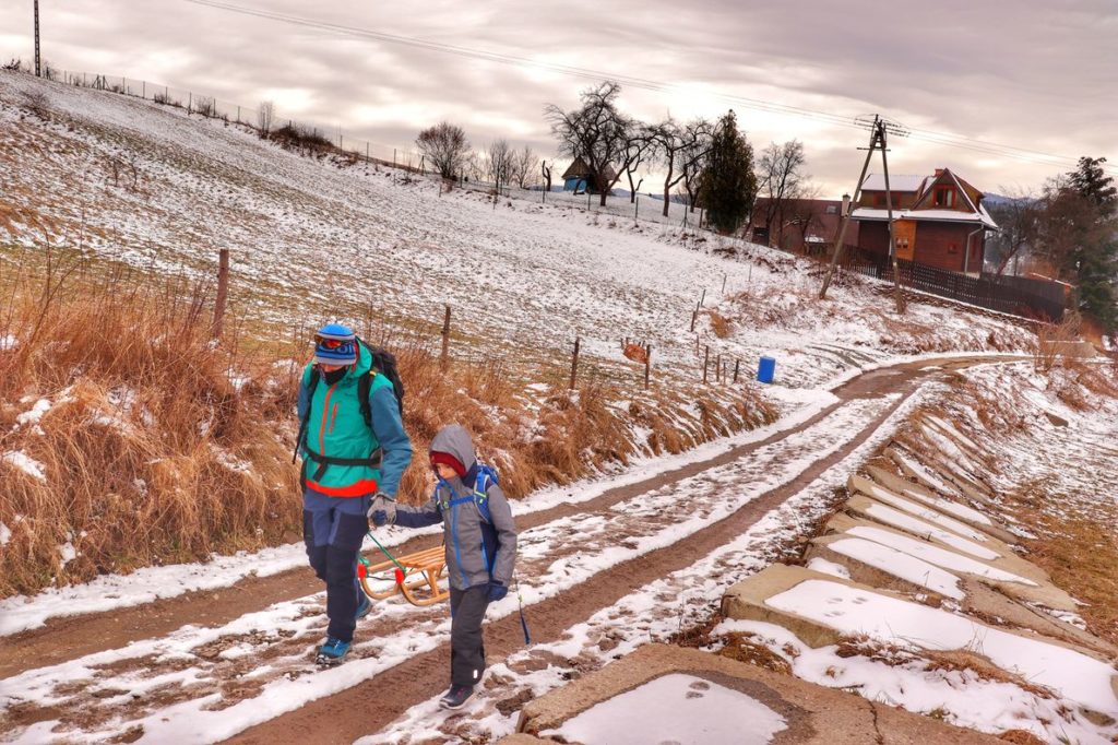 Turysta z dzieckiem, szeroka, miejscami zaśnieżona droga - Rabka Zaryte, w oddali widoczny dom