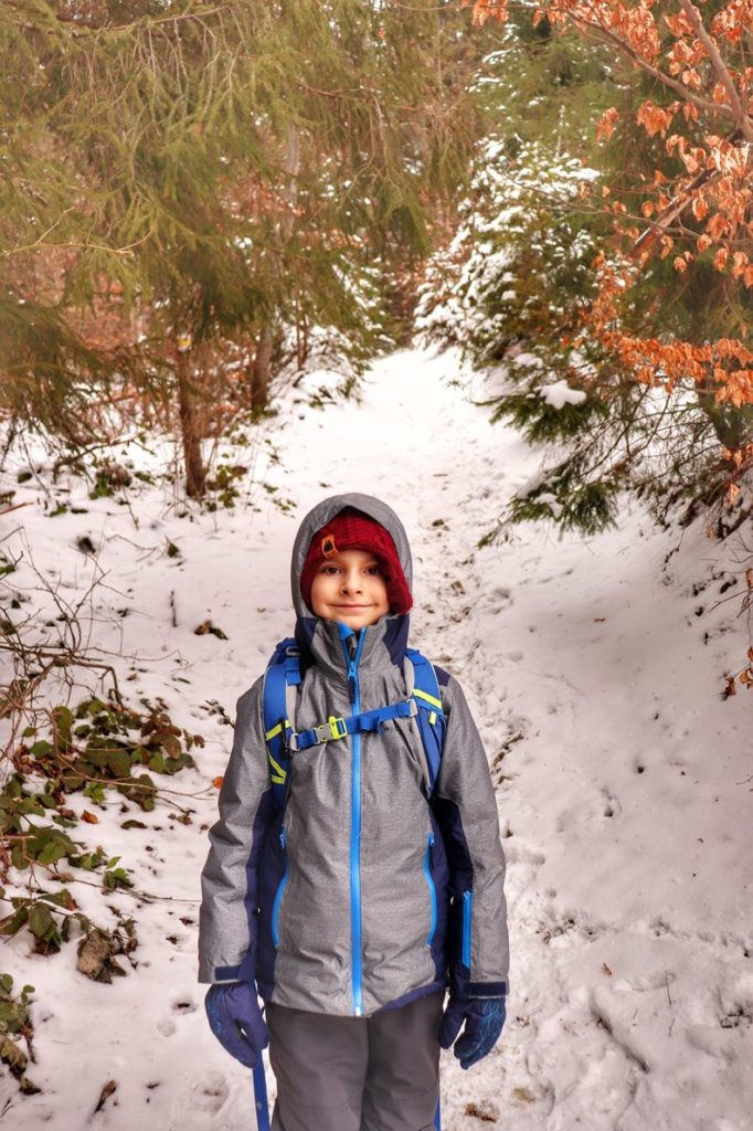 Uśmiechnięte dziecko (chłopiec), leśna ścieżka pokryta śniegiem