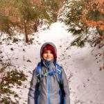 Uśmiechnięte dziecko (chłopiec), leśna ścieżka pokryta śniegiem