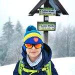 Zadowolone dziecko na Luboniu Wielkim zimą pozujące przy białej tabliczce z napisem Luboń Wielki 1022 m n.p.m.