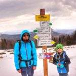 Zadowolony turysta z dzieckiem pozujący przy drewnianym słupie z drogowskazami na Hali Kamińskiego w Beskidzie Żywieckim
