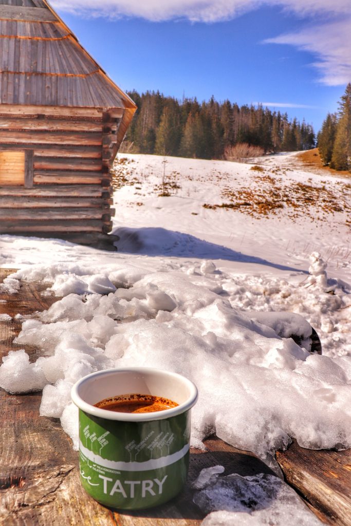 Zielony kubek z napisem TATRY, który jest wypełniony kawą stojący na drewnianym, zaśnieżonym stole na Polanie Olczyskiej