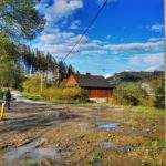 Miejsce skrętu szlaku czarnego w prawo w Soblówce, błotnosta droga, zabudowania, niebieskie niebo, turysta