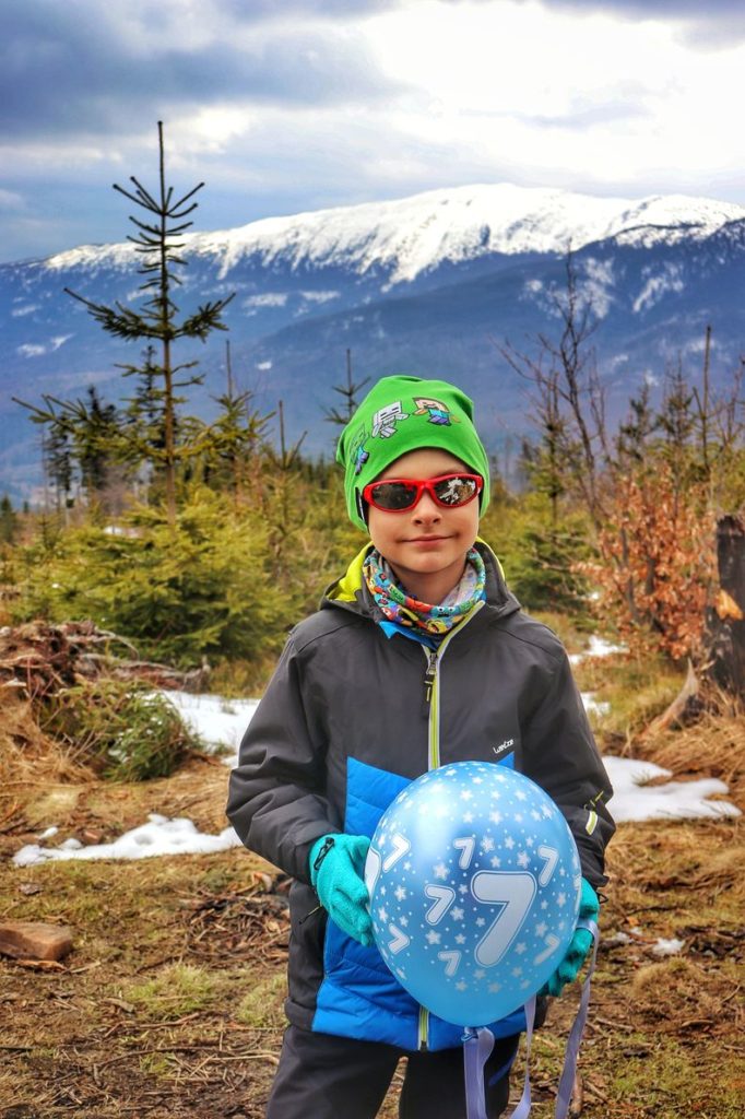 Szczęśliwe dziecko trzymające urodzinowy, niebieski balon, na którym jest cyfra 7, w tle Królowa Beskidów - Babia Góra