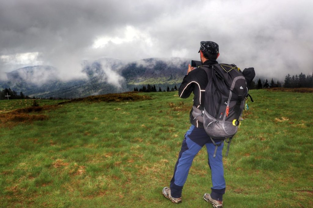 Turysta z wypchanym po brzegi plecakiem turystycznym robiący zdjęcie telefonem komórkowym krajobrazowi górskiemu na Hali Rycerzowej