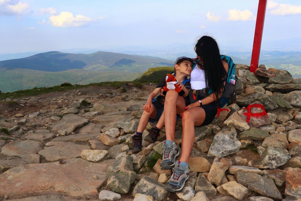 Turystka z dzieckiem odpoczywająca na skałach na czerwonym szlaku na Babią Górę, w tle krajobraz górski