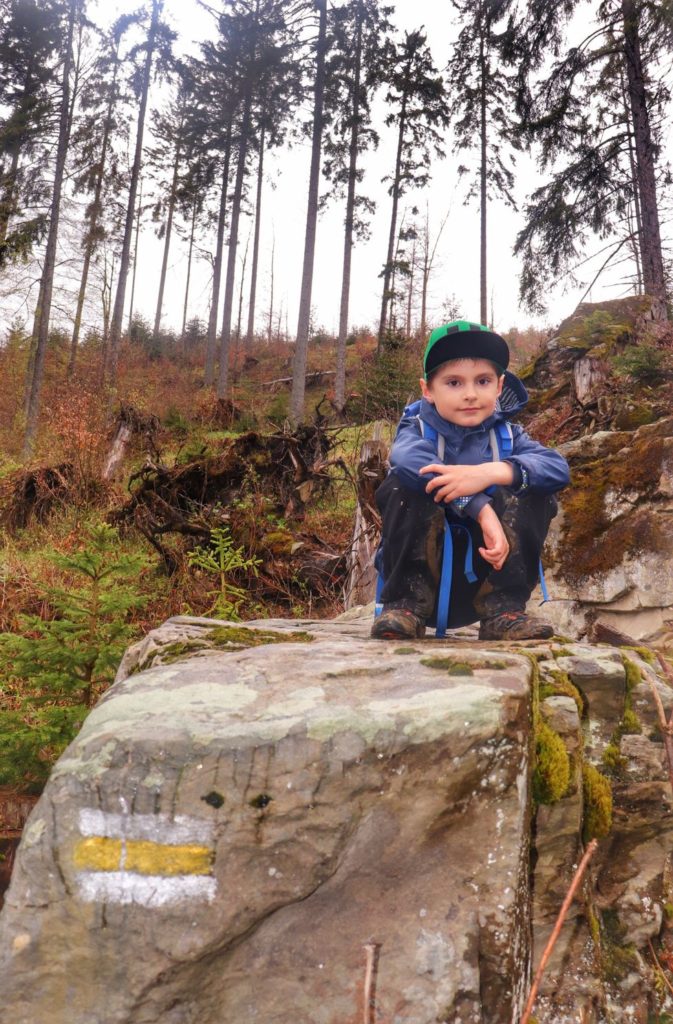 Uśmiechnięte dziecko kucające na skale na żółtym szlaku na Wielką Rycerzową, las