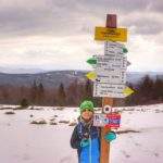 Uśmiechnięte dziecko obejmujące drewniany słup z drogowskazami na Hali Kamińskiego, zimny, wiosenny dzień