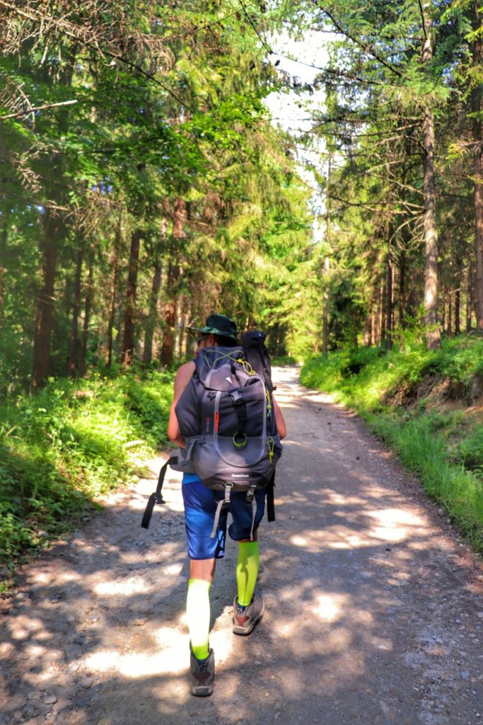 Mężczyzna z wielkim, wypchanym plecakiem turystycznym, szeroka droga leśna w Milówce, letni, słoneczny dzień