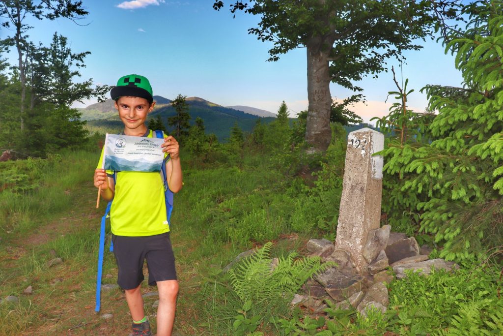 Szczęśliwe dziecko na szczycie Sucha Góra trzymające w rękach chorągiewkę akcji zdobywamy szczyty dla hospicjum