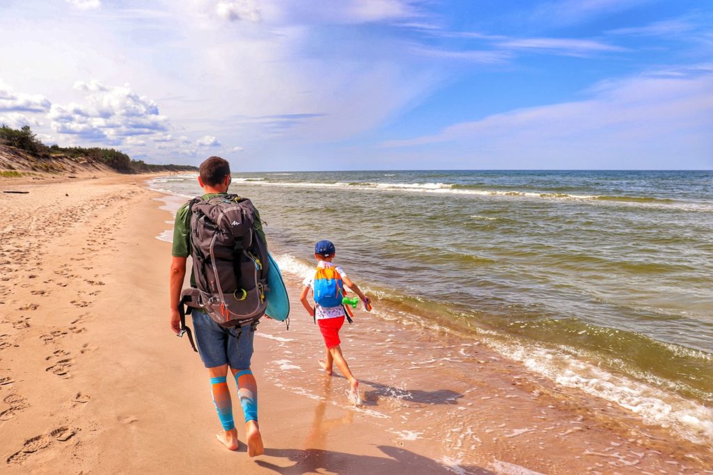 Turysta z dzieckiem idący brzegiem plaży w kierunku Zatopionego Lasu, niebieściutkie niebo