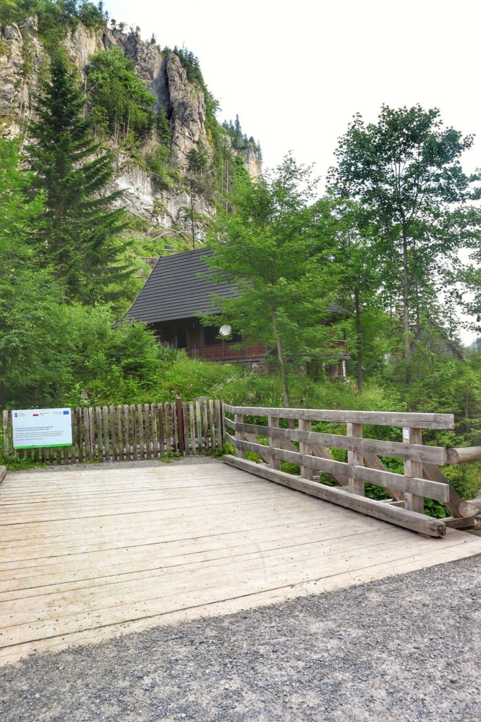 Drewniany mostek nad Chochołowskim Potokiem, za którym widać budynek Leśniczówki