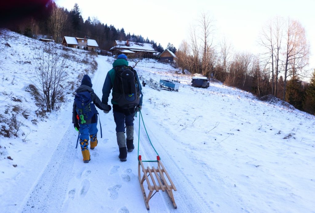 Pokryta śniegiem, pnąca się w górę droga leśna w Milówce, turysta z dzieckiem, w oddali widoczne pojedyncze zabudowania