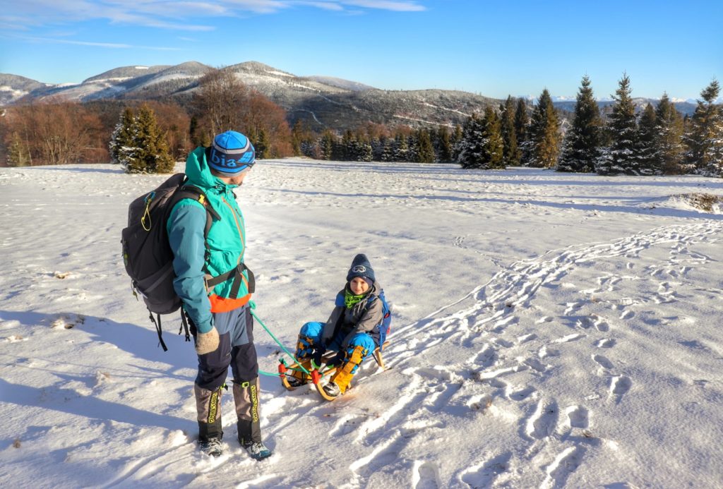 Turysta ciągnący dziecko na siedzące na sankach, zaśnieżona polana Sucha Góra