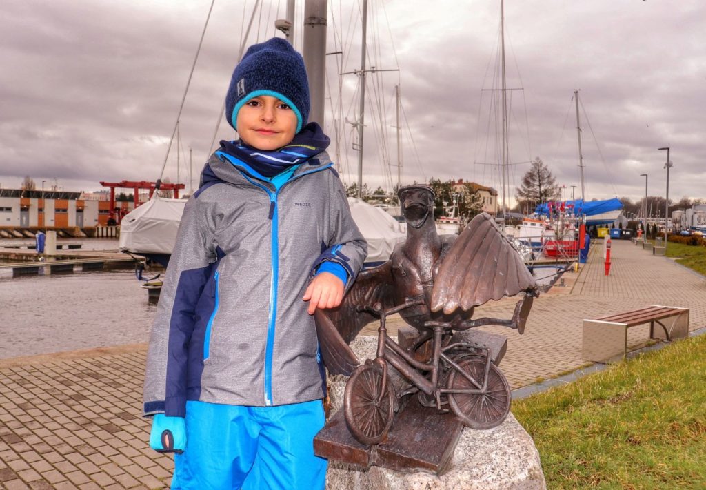 Dziecko stojące przy rzeźbie mewy w Kołobrzegu - Marian wsiadający na rower - Port Jachtowy w Kołobrzegu