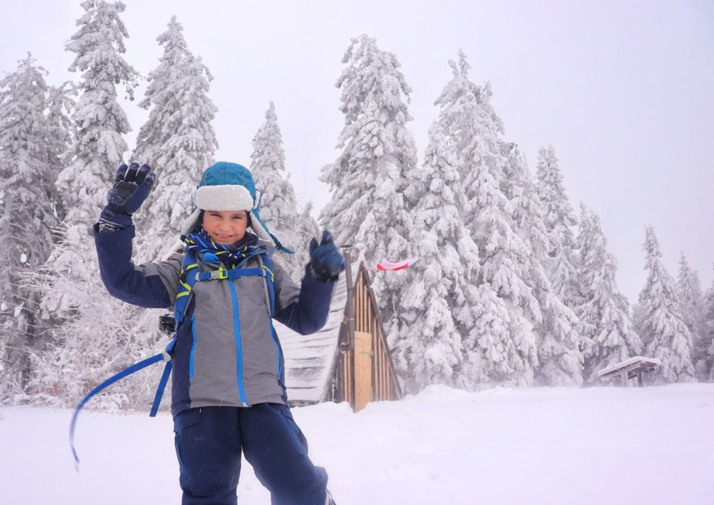 Szczęśliwe dziecko na Jałowcu zimą, w tle drewniana chatka na Jałowcu, zaśnieżone drzewa
