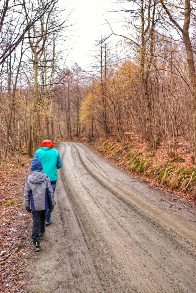 Turysta z dzieckiem idący szeroką drogą leśną w Kozach