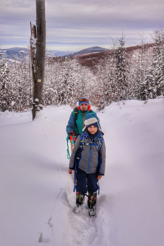 Turyści - mężczyzna z dzieckiem, zaśnieżona ścieżka, szlak żólty na Jałowiec, w tle krajobraz górski