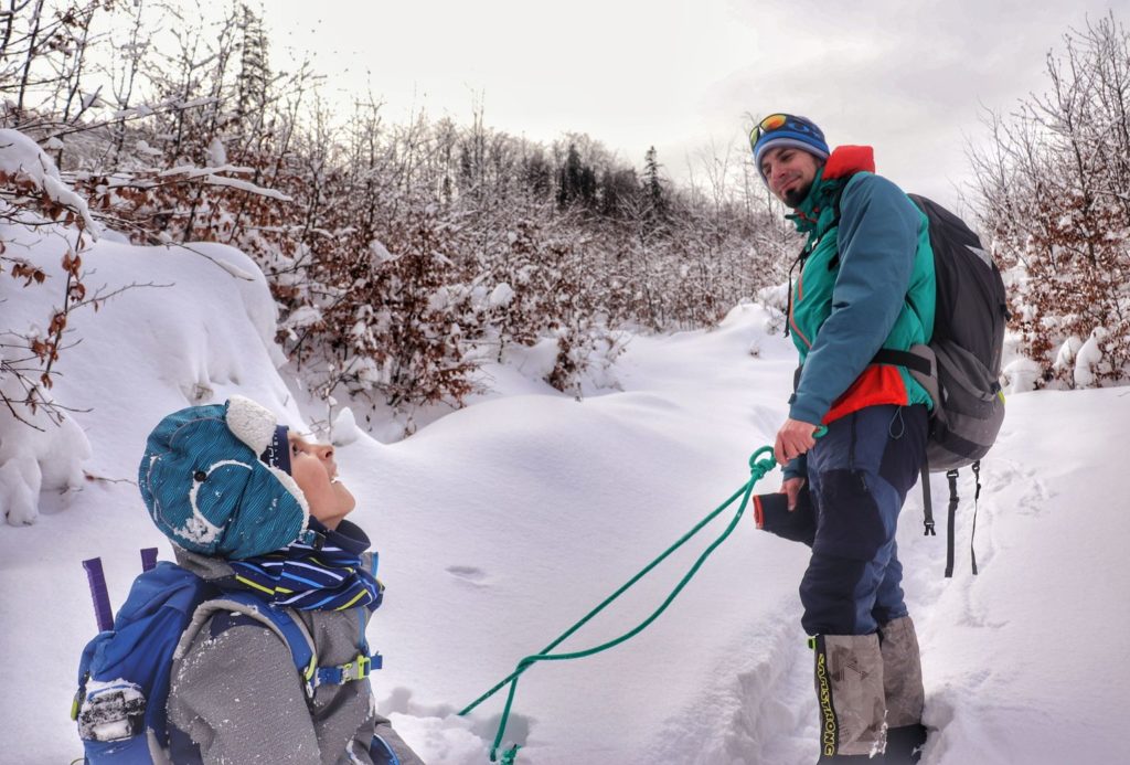 Zadowolone dziecko odpoczywające na sankach, tata trzymający sznur od sanek, zaśnieżona trasa na Jałowiec