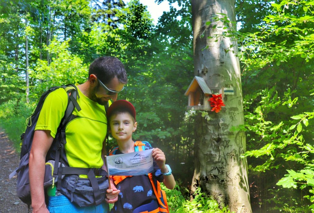 Zadowolony turysta z uśmiechniętym dzieckiem, kapliczka leśna na drzewie na niebieskim szlaku - Pod Bujakowską Górą w Beskidzie Małym