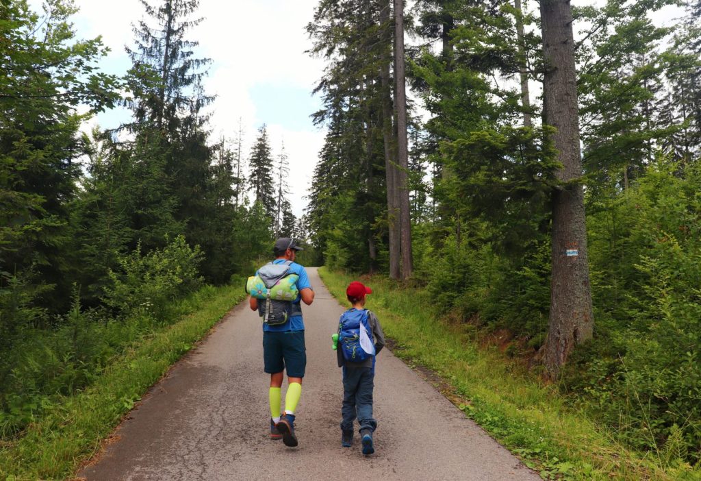 Turysta z dzieckiem na szerokiej asfaltowej drodze leśnej - Koniaków - szlak niebieski