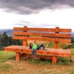 Turystka z dzieckiem odpoczywająca na gigantycznej drewnianej ławce na słowackim szczycie Trojak, letni pochmurny dzień