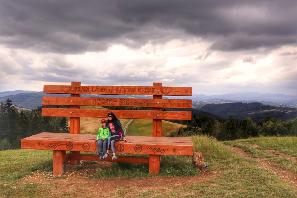 Turystka z dzieckiem siedząca na gigantycznej drewnianej ławce na szczycie Kykula - Słowacja, zachmurzone niebo