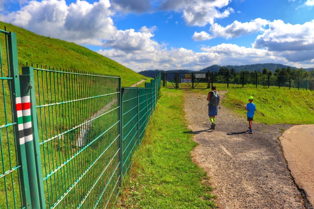 Góra Żar - turysta z dzieckiem na czerwonym szlaku idącym na Kiczerę, zielony płot, szeroka droga