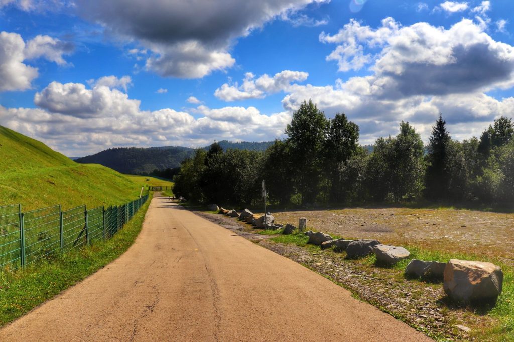 Szeroka asfaltowa droga idąca wzdłuż płotu - szlak czerwony - Góra Żar