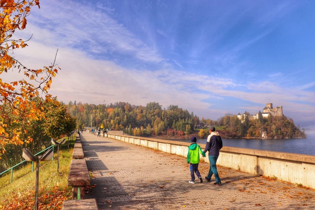 Turyści, mężczyzna i dziecko spacerujący po zaporze w Niedzicy, piękny jesienny poranek, w oddali Zamek Dunajec