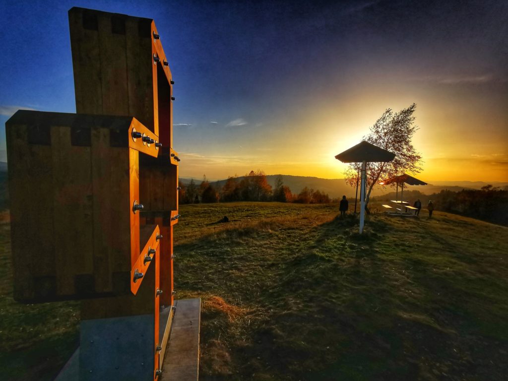Drewniany krzyż, szczyt Gruň w słowackich Beskidach, w tle drewniany stół z zachód słońca