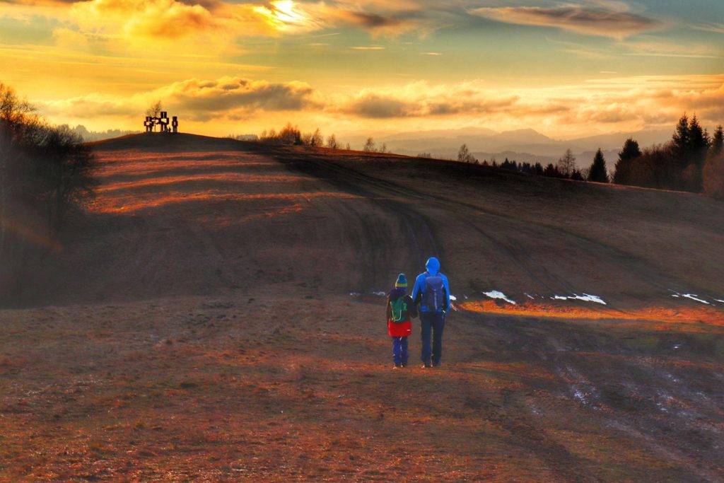 Turysta z dzieckiem na czerwonym szlaku, obszerna polana, w oddali widoczne trzy drewniane krzyże - SKALITSKÉ KRÍŽE - Gruň - zachód słońca