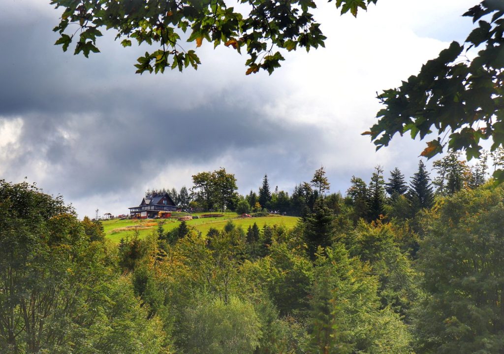 Widok na budynek schroniska na Trzech Kopcach Wiślańskich z zielonego szlaku idącego z Brennej, zachmurzone niebo