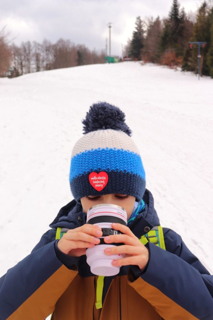 Szyndzielnia zimą, dziecko pijące ciepłą herbatę z białego kubka