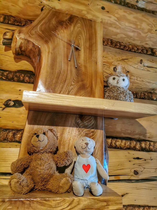 Drewniany zegar z pułkami, na których leżą pluszowe zabawki - miś, sowa wiszące w schronisku pod Durbaszką