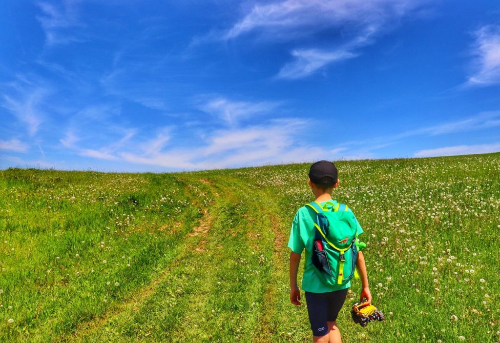 Mały turysta, dziecko idące wzdłuż polany w Pieninach Spiskich, maj, niebieskie niebo