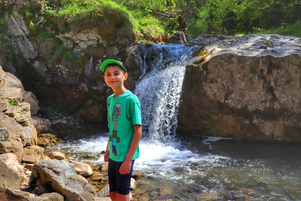 Uśmiechnięte dziecko na tle wodospadu w Rezerwacie Przyrody Biała Woda