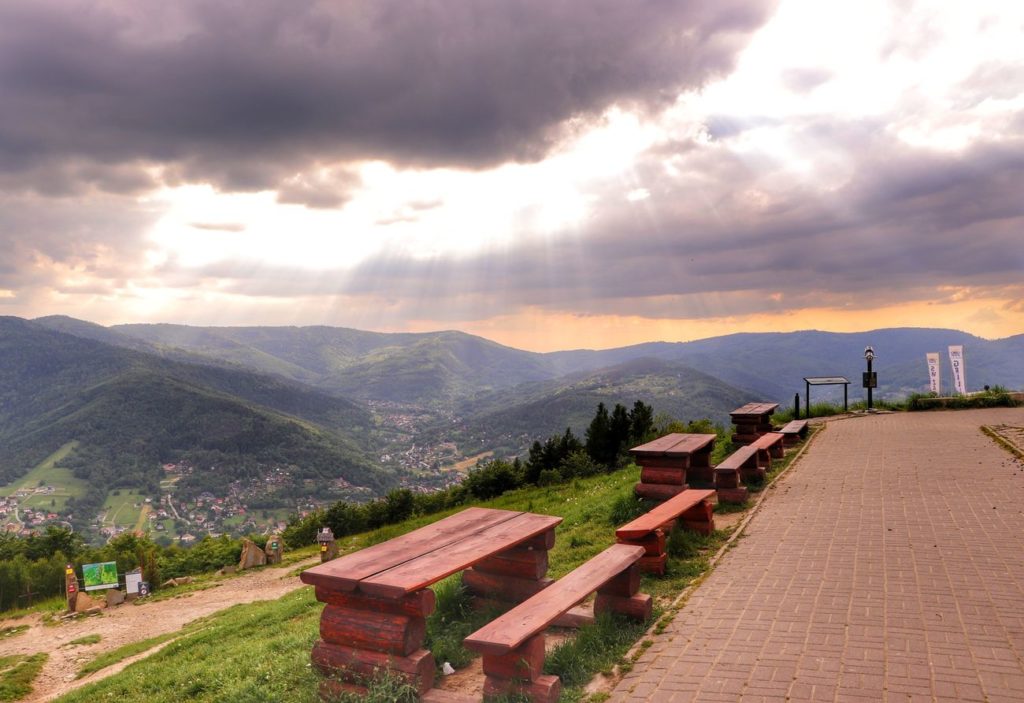 Widok rozciągający się z Góry Żar, brukowany chodnik, drewniane stoły i ławki