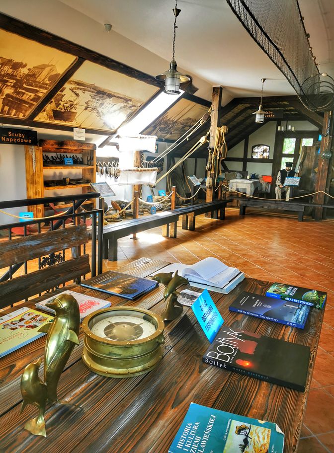 Drewniany stół, atlasy, książki, pomieszczenie w Galerii Rybackiej w Jezierzanach koło Jarosławca