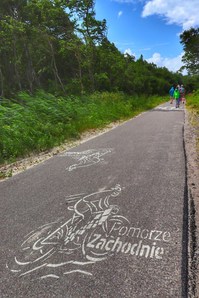 Droga asfaltowa, rysunek rowerzysty z napisem Pomorze Zachodnie, szlak rowerowy - Mierzeja nad Jeziorem Kopań