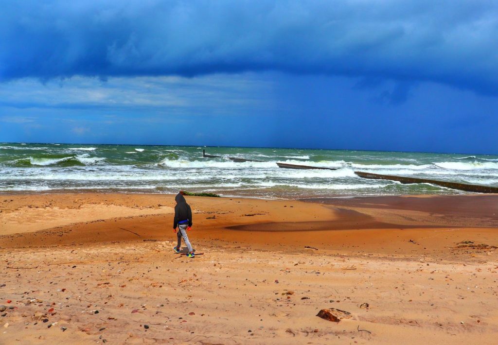 Dziecko spacerujące po pustej plaży, zachmurzone niebo o pięknym niebieskim kolorze