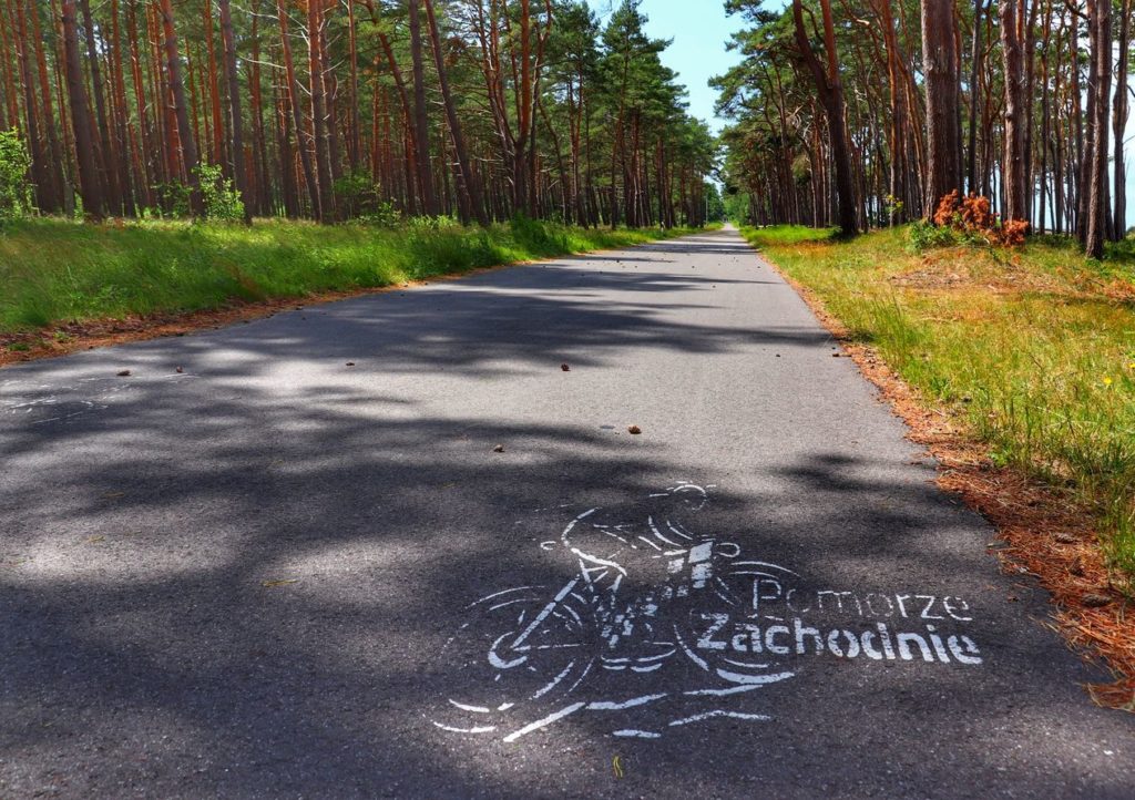 Mierzeja na Jeziorze Kopań, szeroka asfaltowa droga, na której naniesiona jest postać rowerzysty z napisem Pomorze Zachodnie