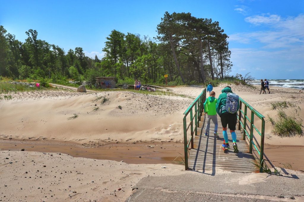 Turysta z dzieckiem przechodzący przez mostek w miejscu połączenia Jeziora Kopań z Morzem Bałtyckim