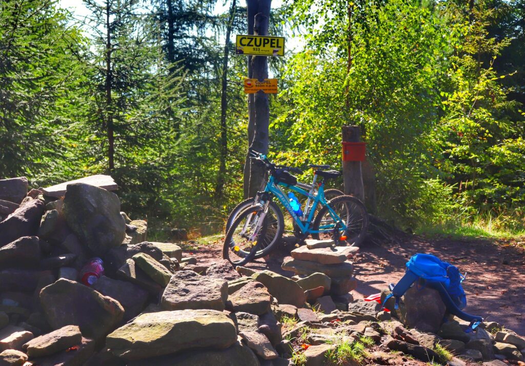 Szczyt Czupel w Beskidzie Małym, rowery, słup z żółtą tabliczką oznaczającą szczyt Czupel, kamienie