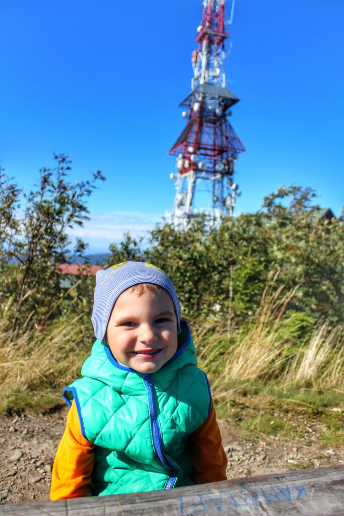 Uśmiechnięte dziecko szczyt Skrzyczne w Beskidzie Śląskim, w tle nadajnik telewizyjny, niebieskie niebo